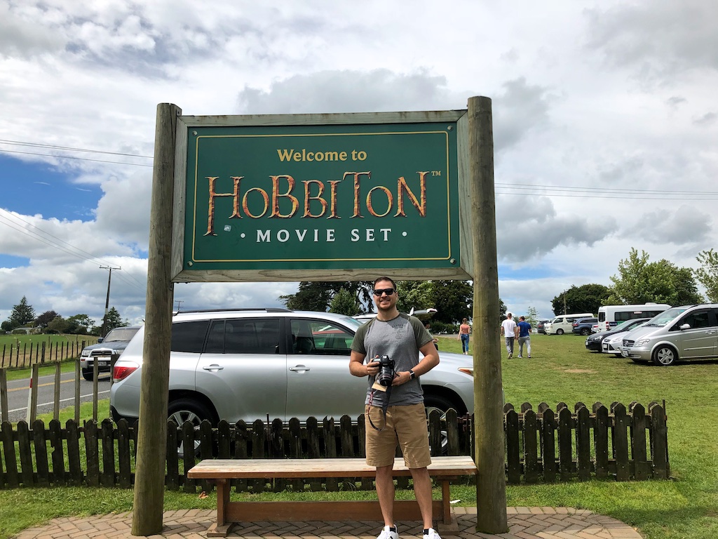 Man standing under Hobbiton movie set sign