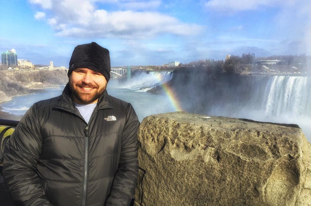 Man standing next Niagara Falls with rainbow