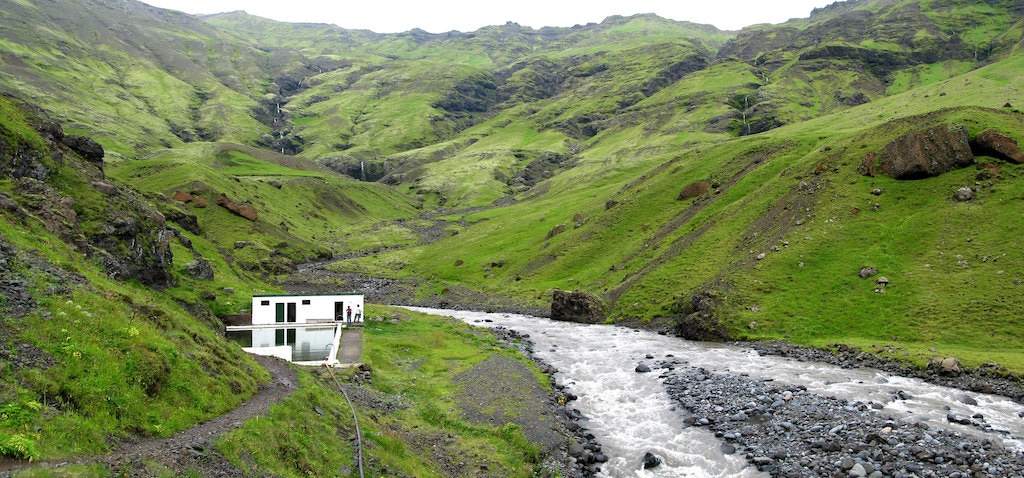 Grass covered mountain with creek at Seljavallalaug