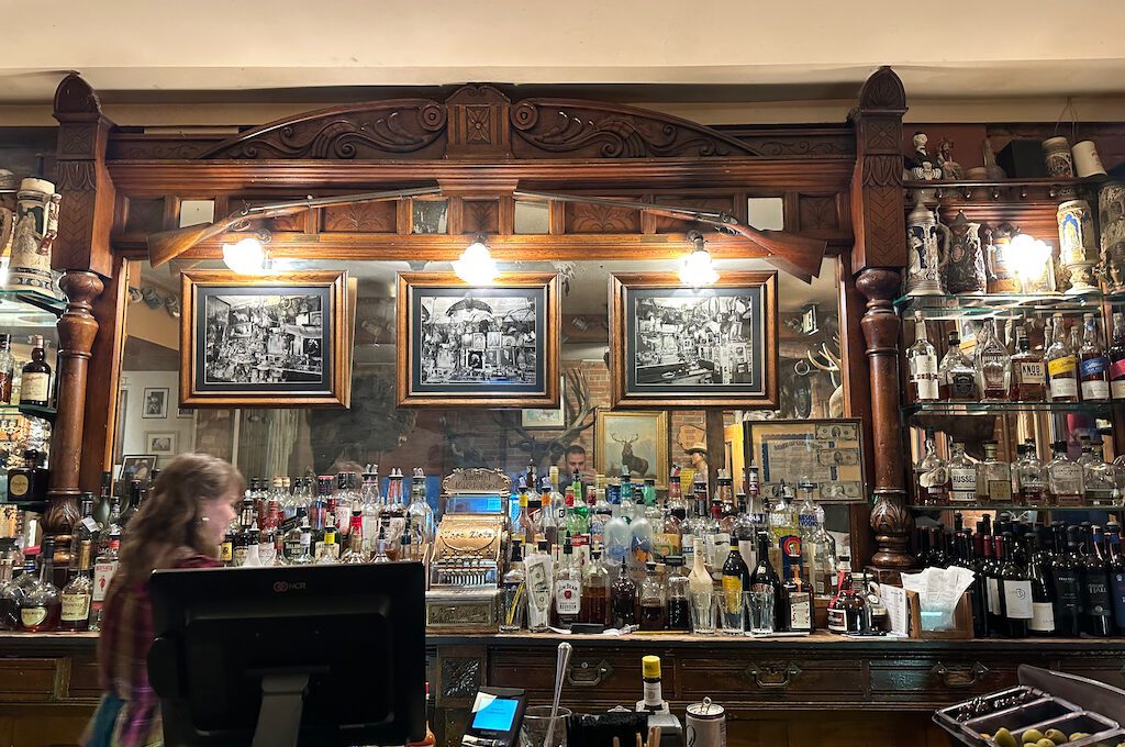 A bar with a counter and a bar with bottles and a person behind it