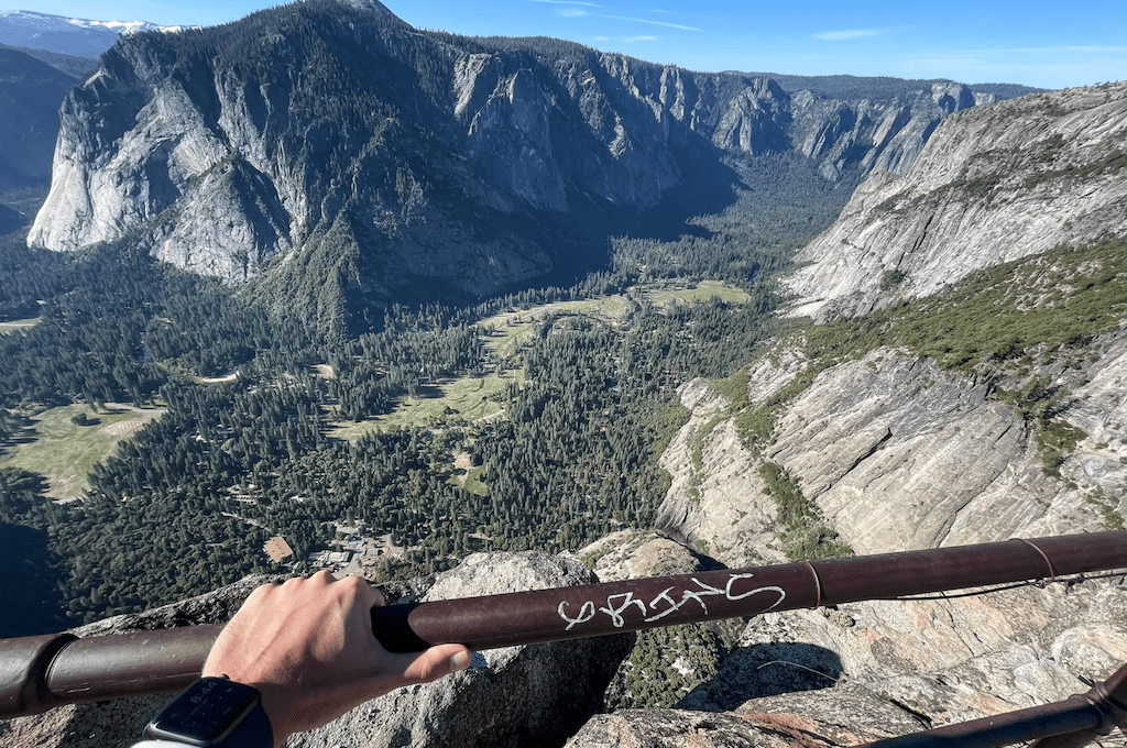Hand gripping metal railing with mountains in the distance