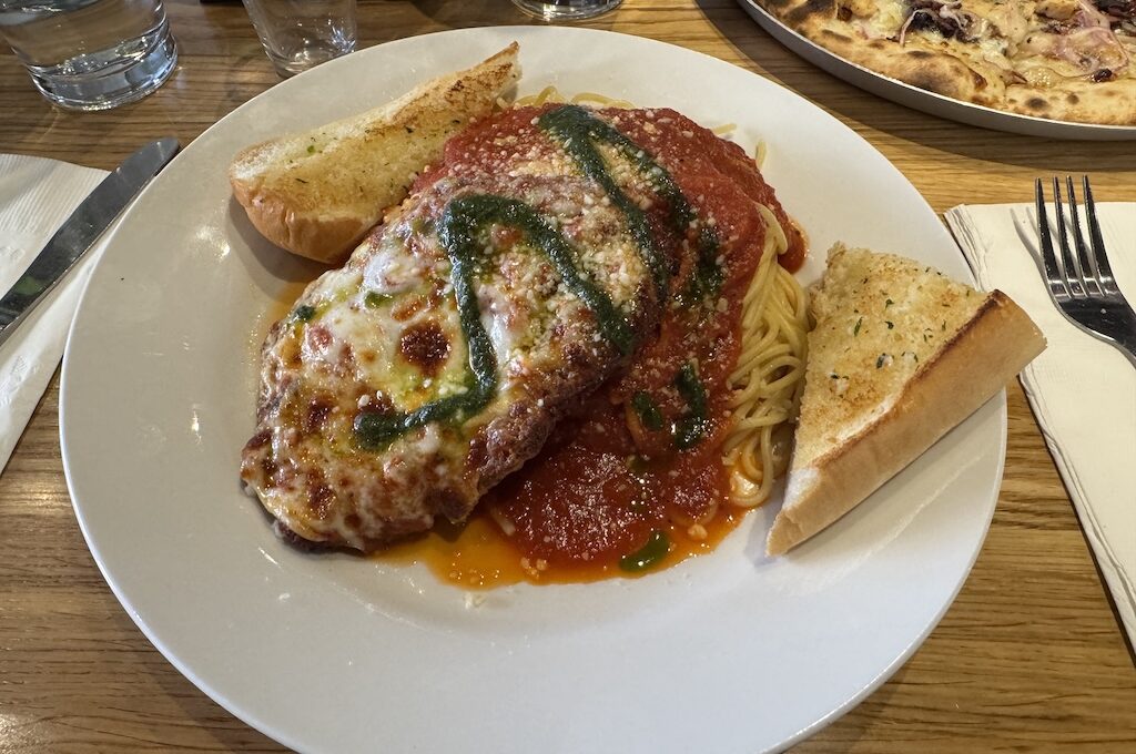 Chicken parmesan with green drizzle, spaghetti and garlic bread