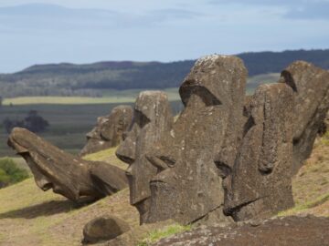 A row of partially buried moai statues on a grassy slope at Rano Raraku, with distant hills in the background
