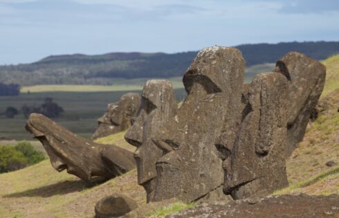 A row of partially buried moai statues on a grassy slope at Rano Raraku, with distant hills in the background