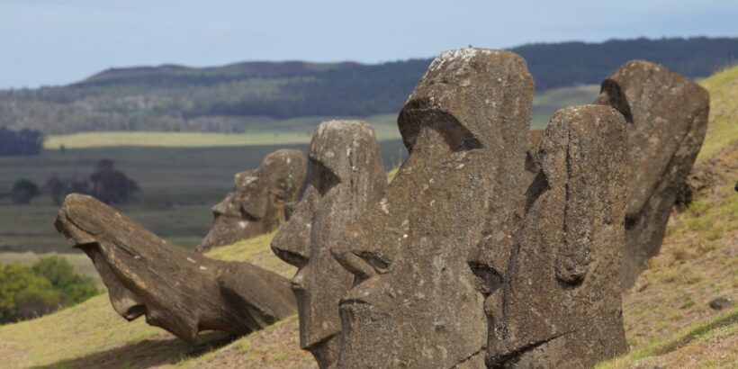 A row of partially buried moai statues on a grassy slope at Rano Raraku, with distant hills in the background
